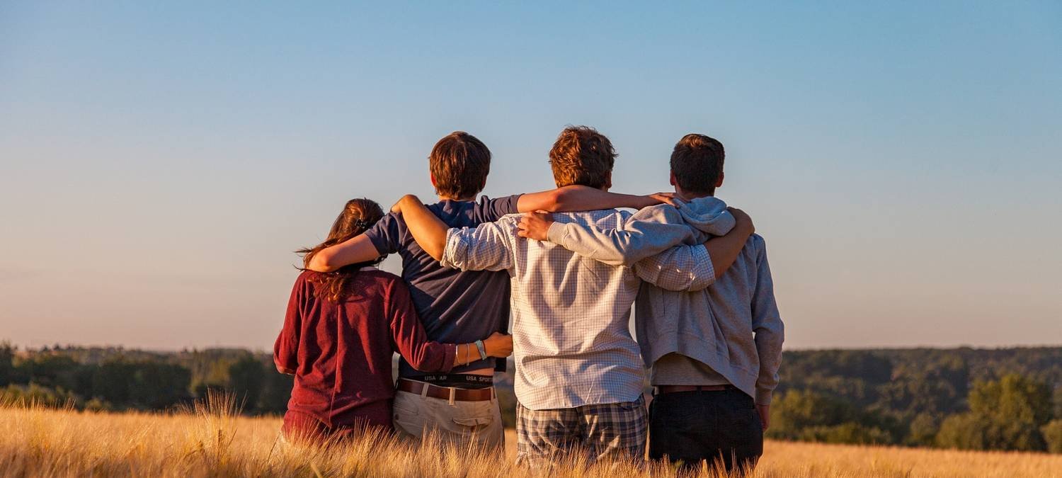 Friends with arms around each other looking over a golden field at sunset